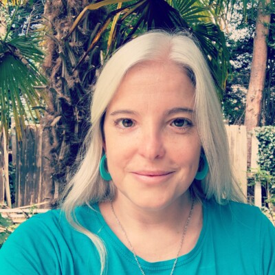 Photo of Sara Erddig sat outside. She is smiling at the camera and is wearing a blue top.