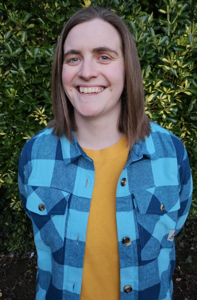 Photo of Hilary Watson. She is standing outside and is smiling broadly at the camera.