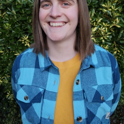 Photo of Hilary Watson. She is standing outside and is smiling broadly at the camera.