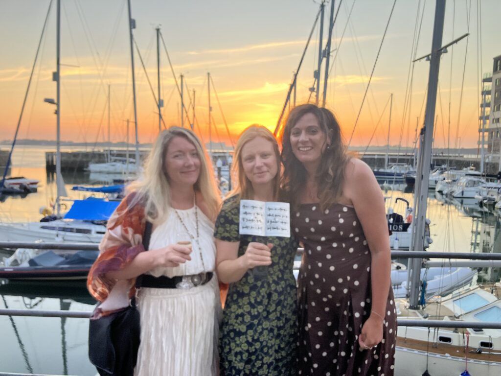 Photo of Zoe, Laura and Bronwen standing in front of the harbour with Laura's award.