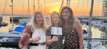 Photo of Zoe, Laura and Bronwen standing in front of the harbour with Laura's award.