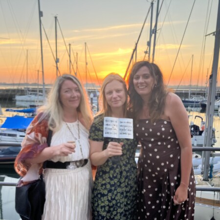 Photo of Zoe, Laura and Bronwen standing in front of the harbour with Laura's award.