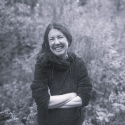 Black and white photo of Julie Brominicks standing outside. She is smiling at the camera with her arms crossed.
